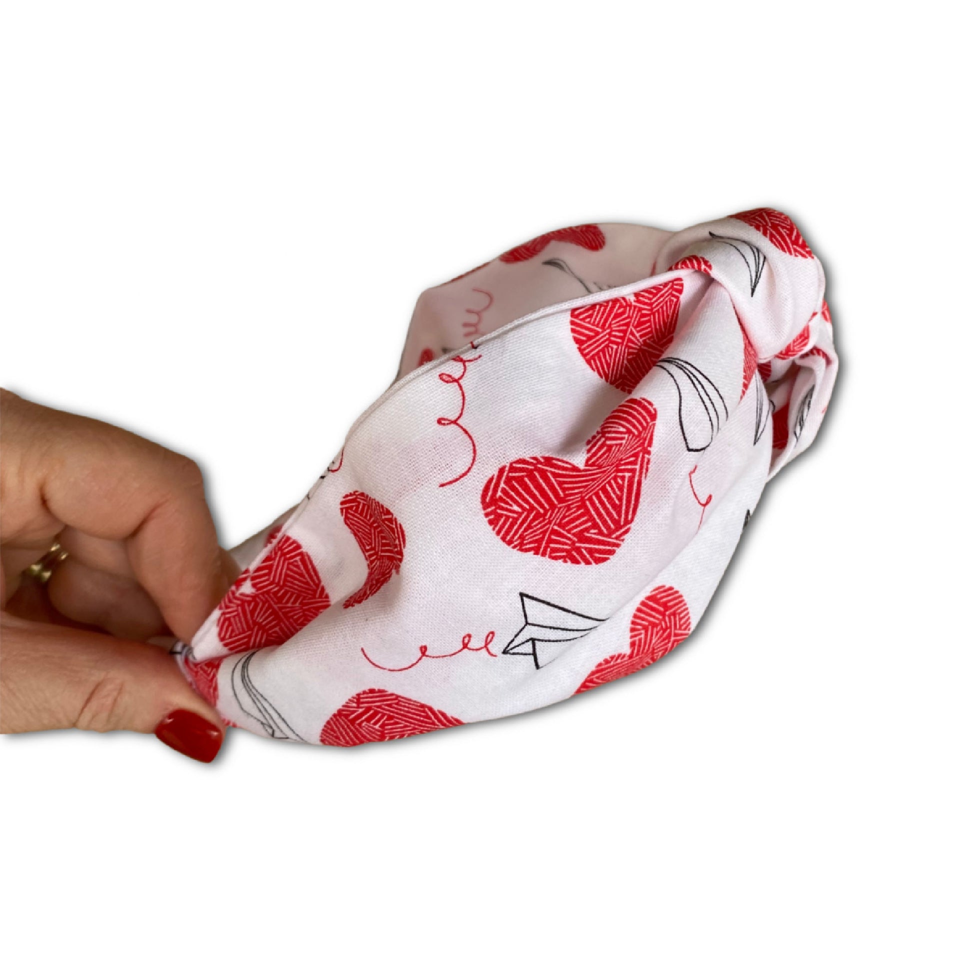 headband that has a knot at top. made with a cotton print that is white with red large hearts and paper airplane outlines